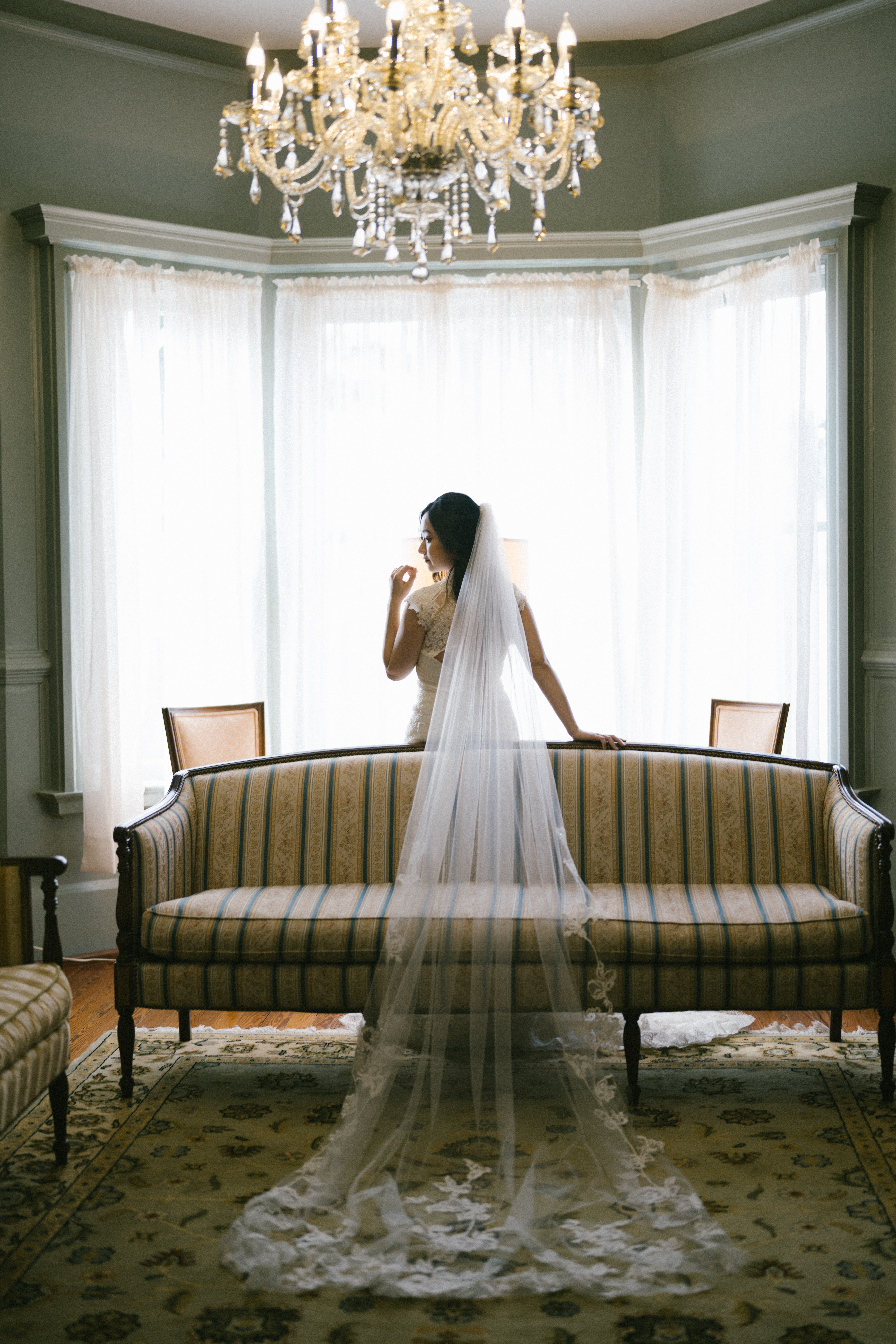 bride in long lace veil gazing out windows under chandelier