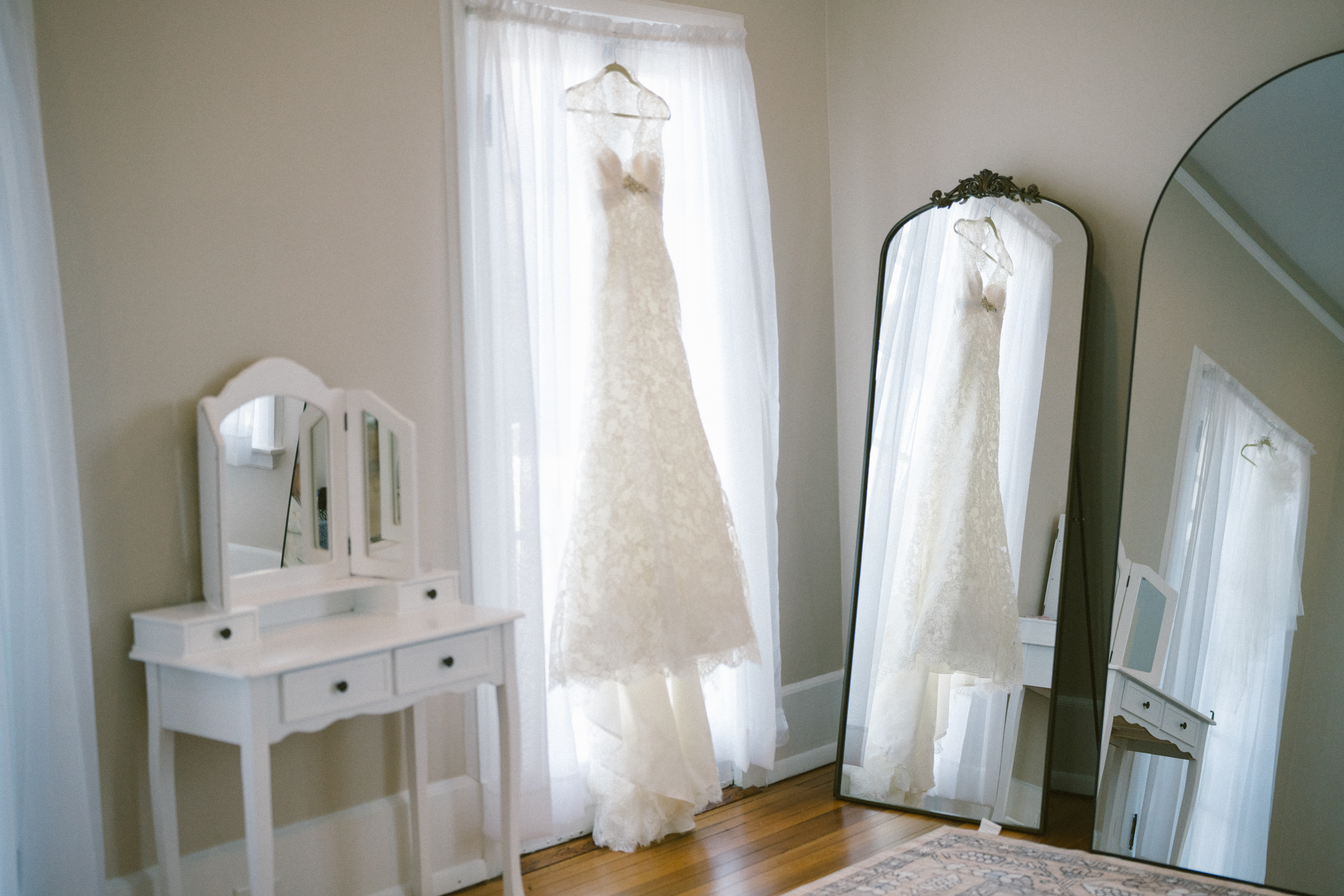 wedding gown hanging in window reflection in antique mirror